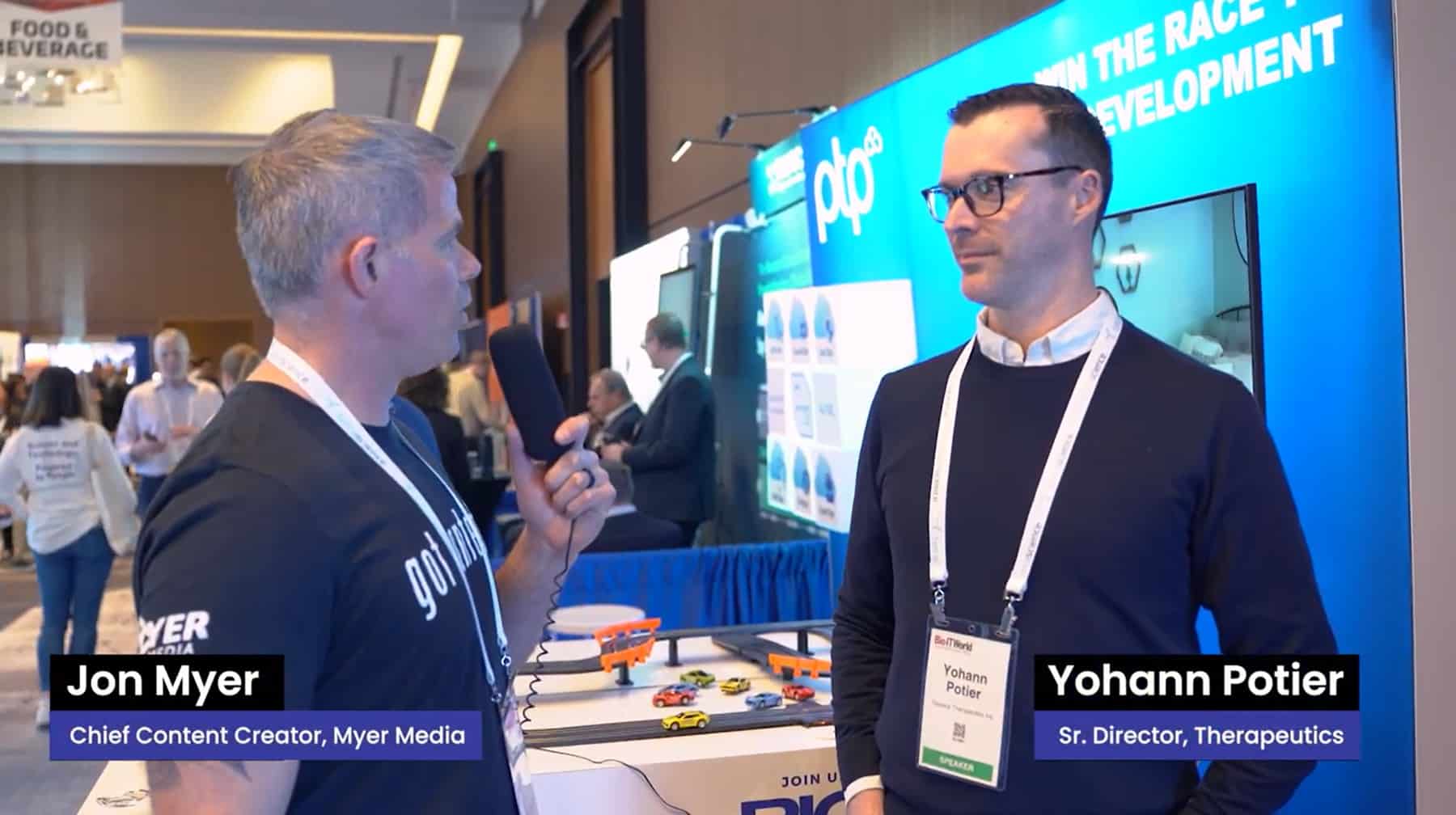 Yohann Potier being interviewed at the PTP booth during Bio-IT World 2024, with the conference setting visible in the background.