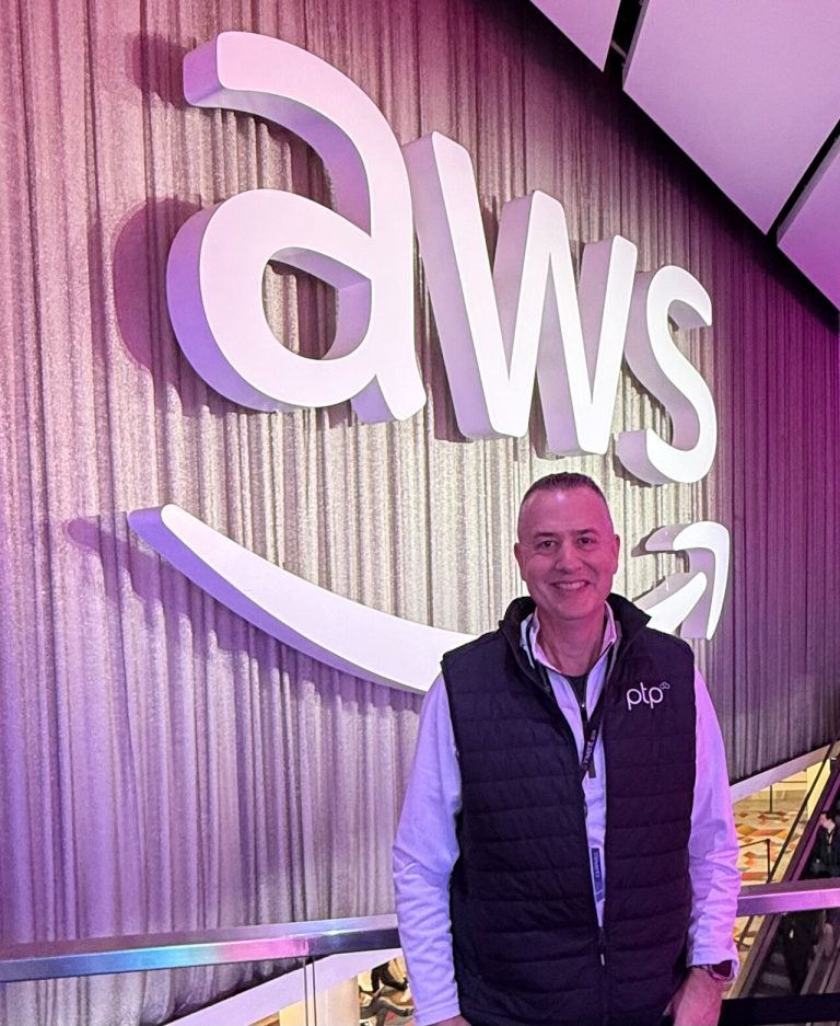 Ethan Simmons, a representative of PTP, standing in front of a large illuminated AWS logo at AWS re:Invent 2024.