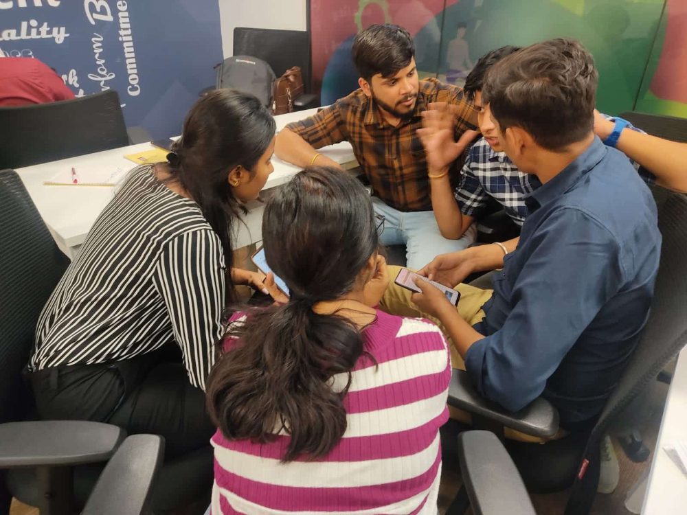 Group of coworkers sitting together in an office, collaborating and discussing something on their phones and notebooks.